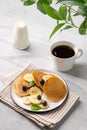 Delicious banana pancakes with fresh fruit slices, berries, mint and honey on a light background with a cup of black coffee, milk Royalty Free Stock Photo