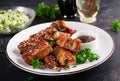 Delicious barbecued spare ribs on plate on dark background.