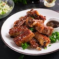 Delicious barbecued spare ribs on plate on dark background.