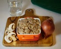 Delicious Beef stroganoff in a ceramic bowl decorated an onion, mushrooms a glass of water and a napkin on a cutting board
