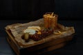 Delicious beef tar-tar with white baguette slices and french fries with pickled cucumber on a wooden board stands on a table