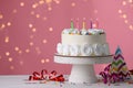 Delicious birthday cake and party decor on white wooden table against blurred festive lights, space for text Royalty Free Stock Photo