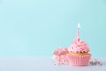 Delicious birthday cupcake with burning candle, sprinkles and gift box on white table against turquoise background, space for text Royalty Free Stock Photo
