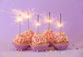 Delicious birthday cupcakes with firework candles on color background Royalty Free Stock Photo