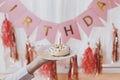 Delicious birthday donut with candle in hand on background of pink garland and decorations in room