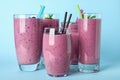 Delicious blackberry smoothie in different glassware on blue background