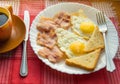 Delicious Breakfast - a Cup of coffee, a plate of fried eggs, bacon and toast, next to the Cutlery on red checkered napkin