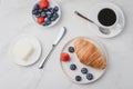 Delicious breakfast with fresh berries. Coffee cup, creamer and croissant with berries in white bowl and butter on table. Top view Royalty Free Stock Photo