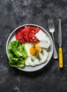 Delicious breakfast, snack, tapas - fried egg, ripe tomatoes, greek cheese, green salad on a dark background, top view Royalty Free Stock Photo