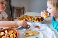 Delicious breakfast with tiny mini pancakes, cherries, apricots, jam on a white table. Small children hold pancakes in