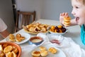 Delicious breakfast with tiny mini pancakes, cherries, apricots, jam on a white table. Small children hold pancakes in