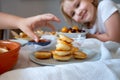 Delicious breakfast with tiny mini pancakes, cherries, apricots, jam on a white table. Small children hold pancakes in