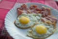 Delicious Breakfast - white plate of fried eggs, bacon on a red napkin Royalty Free Stock Photo