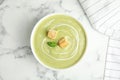 Delicious broccoli cream soup with croutons served on marble table, top view