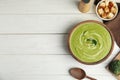 Delicious broccoli cream soup served on white wooden table, flat lay. Space for text