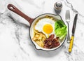 Delicious brunch, breakfast - potatoes hash, fried egg, bacon and green salad in a frying pan on a light background, top view Royalty Free Stock Photo