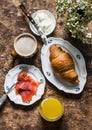 Delicious brunch - cappuccino, croissant, cream cheese, smoked salmon, orange juice on a wooden background, top view