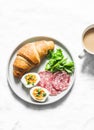 Delicious brunch - croissant, boiled egg, salami sausage, green salad and coffee with milk on a light background