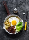 Delicious brunch - hash potatoes, fried egg, bacon and green salad in a frying pan on a dark background, top view Royalty Free Stock Photo