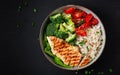 Delicious buddha bowl with grilled chicken, fresh vegetables and rice on a dark background. Top view, above Royalty Free Stock Photo