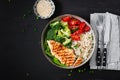 Delicious buddha bowl with grilled chicken, fresh vegetables and rice on a dark background. Top view, above Royalty Free Stock Photo