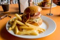 Delicious burger with bacon, cheese, chicken and french fries potato chips on side on the table at the cafe Royalty Free Stock Photo