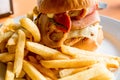 Delicious burger with bacon, cheese, chicken and french fries potato chips on side on the table at the cafe Royalty Free Stock Photo