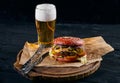 Delicious burger with beer and french fries on a wooden rustic table. Gamberger with salom onion and meat cutlet with a Royalty Free Stock Photo
