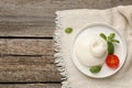 Delicious burrata cheese with basil and tomato on wooden table, top view. Space for text
