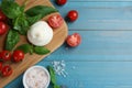 Delicious burrata cheese with basil and tomatoes on light blue wooden table, flat lay. Space for text