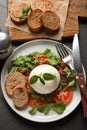 Delicious burrata salad with tomatoes, arugula and pesto sauce served on black table, flat lay