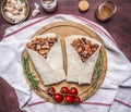 Delicious burrito with meat, beans, and vegetables on a cutting board and a napkin with cherry tomatoes and garlic on wooden rusti