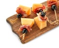 Delicious canape with melon, prosciutto and olives on wooden board against white background