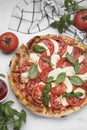 Delicious Caprese pizza with tomatoes, mozzarella and basil served on white table, flat lay