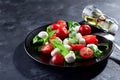 Delicious caprese salad with ripe cherry tomatoes and mini mozzarella cheese balls with fresh basil leaves on black Royalty Free Stock Photo