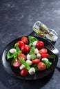 Delicious caprese salad with ripe cherry tomatoes and mini mozzarella cheese balls with fresh basil leaves on black Royalty Free Stock Photo