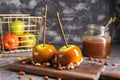 Delicious caramel apples with tree branches on wooden board