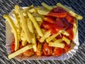 Delicious cardboard plate filled with ketchup-coated fries accompanied by currywurst, a German culinary specialty, to eat outdoors