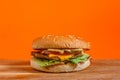 Delicious cheeseburger with lettuce, tomato, cheese, and bacon on a wooden surface. Studio shot with orange background