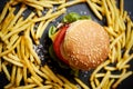 Delicious cheeseburger surrounded by french fries on a black table