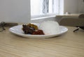 Delicious chicken rice with fried noodles and spicy chili sauce, served on a white plate on a restaurant table. Royalty Free Stock Photo