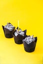 Delicious chocolate cupcakes with cream and candle on yellow background. Three chocolate muffin. Birthday cake party. Royalty Free Stock Photo