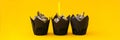 Delicious chocolate cupcakes with cream and candle on yellow background. Three chocolate muffin. Birthday cake party. Royalty Free Stock Photo