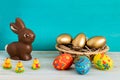 Happy Easter concept with color ang gold aster eggs in basket next to chocolate Easter bunny and baby chicken on blue wooden backg Royalty Free Stock Photo