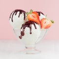 Delicious classic creamy ice cream scoops in bowl with strawberry slices, chocolate sauce in modern pink interior on white wood.