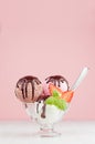 Delicious classic different color ice cream scoops in bowl with mint, spoon, chocolate sauce, strawberry slices in pink interior