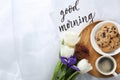 Delicious coffee, cookies, flowers and GOOD MORNING wish on white cloth. Space for text