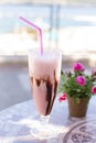 Delicious cold milk dessert with chocolate and strawberries in a glass goblet with a straw on a ceramic table and flowers, blurred Royalty Free Stock Photo