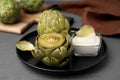 Delicious cooked artichokes with tasty sauce served on grey wooden table, closeup