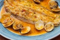 Delicious cooked clams and halibut in a buttery sauce on a plate.